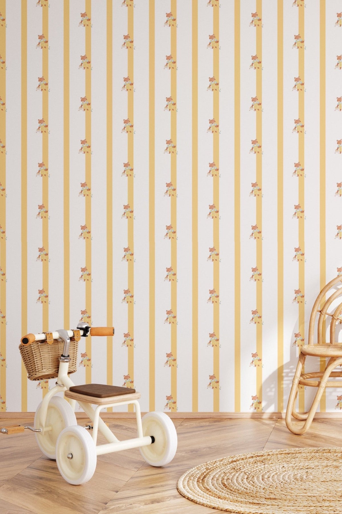 Échantillon du papier peint Joy à rayures jaunes et illustrations de petits renards, posé dans une chambre d'enfant avec un tricycle vintage blanc, une chaise en rotin et un tapis rond en jute.