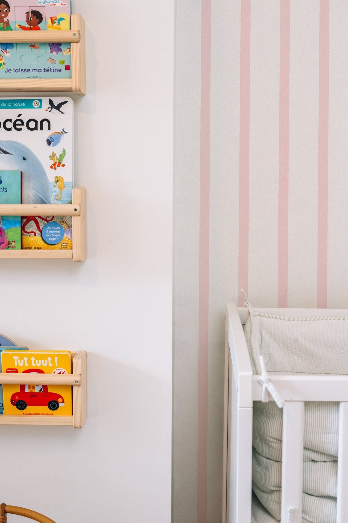 Échantillon du papier peint Rosie à rayures roses, posé derrière des étagères à livres en bois et un lit d'enfant blanc.