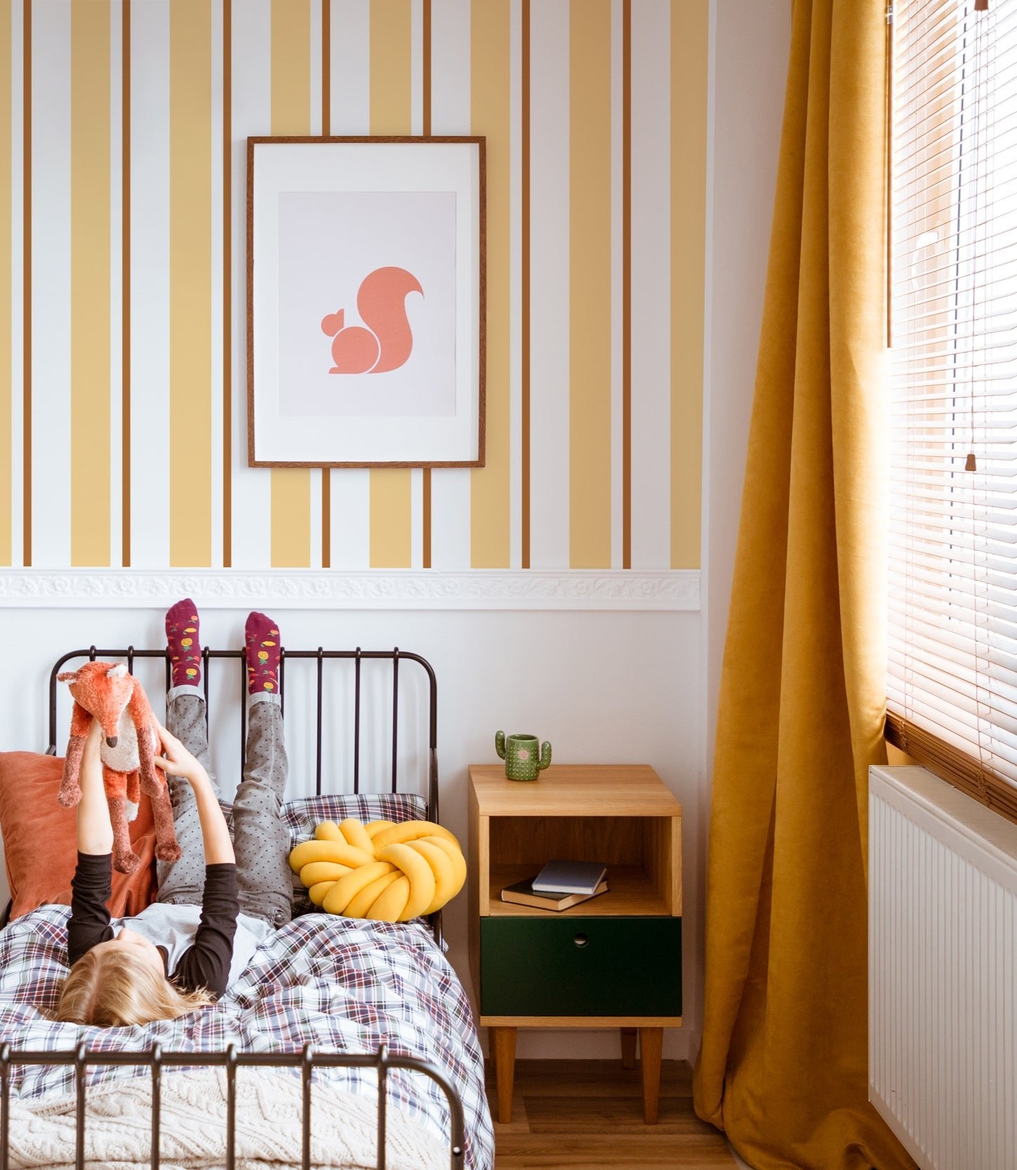Papier peint Daphné à rayures, posé au-dessus d'une moulure dans une chambre d'enfant avec un lit en fer forgé.