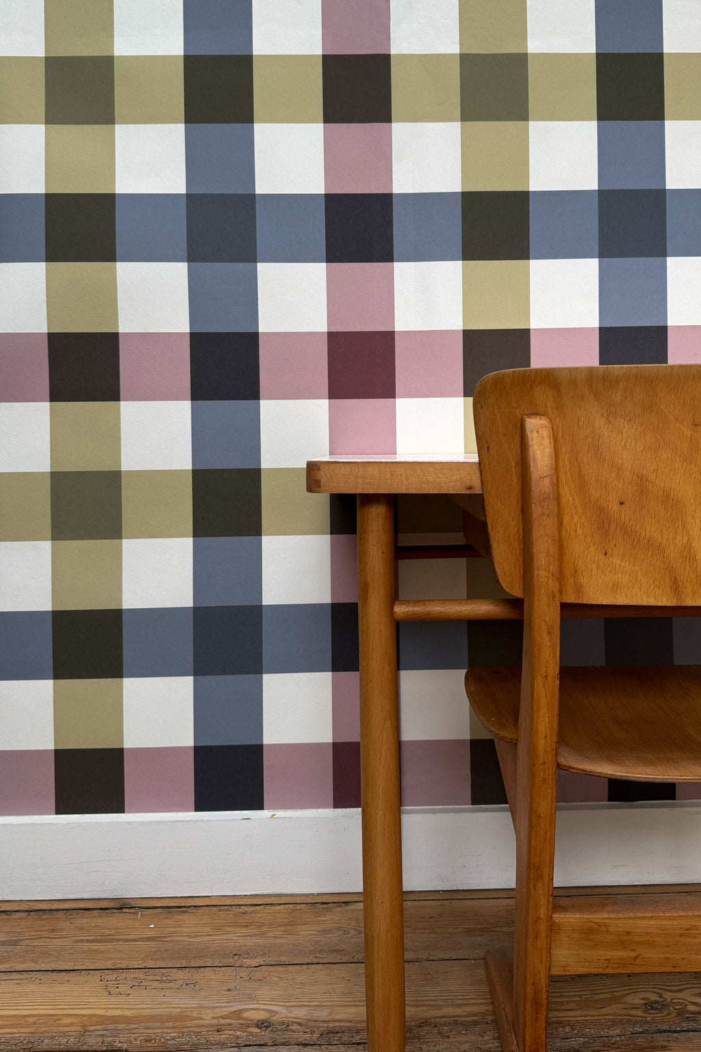 Papier peint Harold à grands carreaux croisés bleu, vert olive et vieux rose, mis en valeur derrière un bureau d'écolier et une chaise en bois vintage.