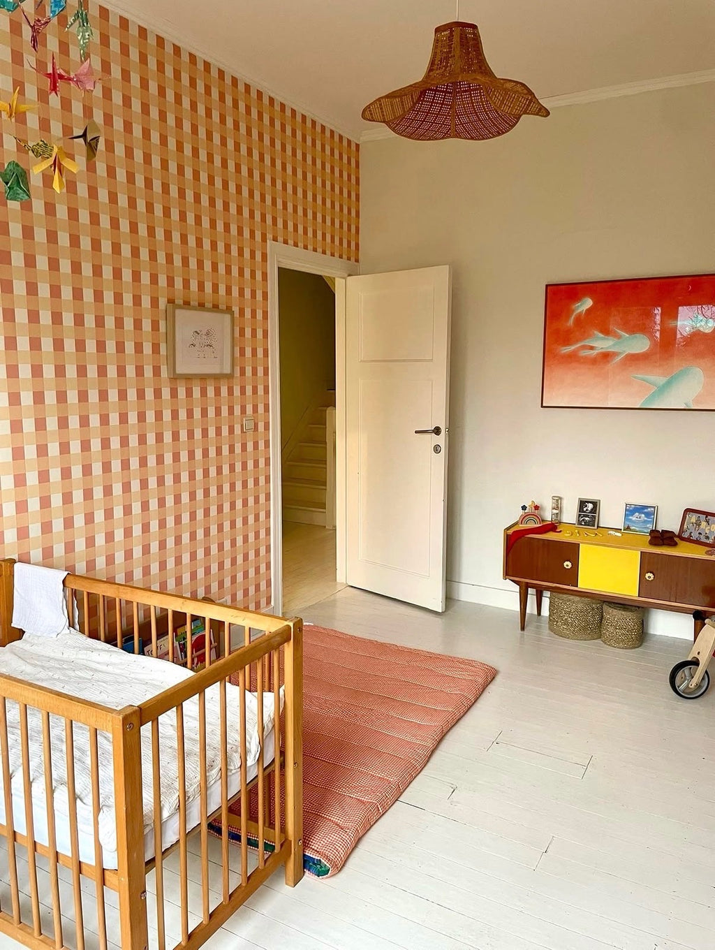 Décoration de chambre de bébé avec papier peint Jim à carreaux vichy orange, berceau en bois et luminaire.