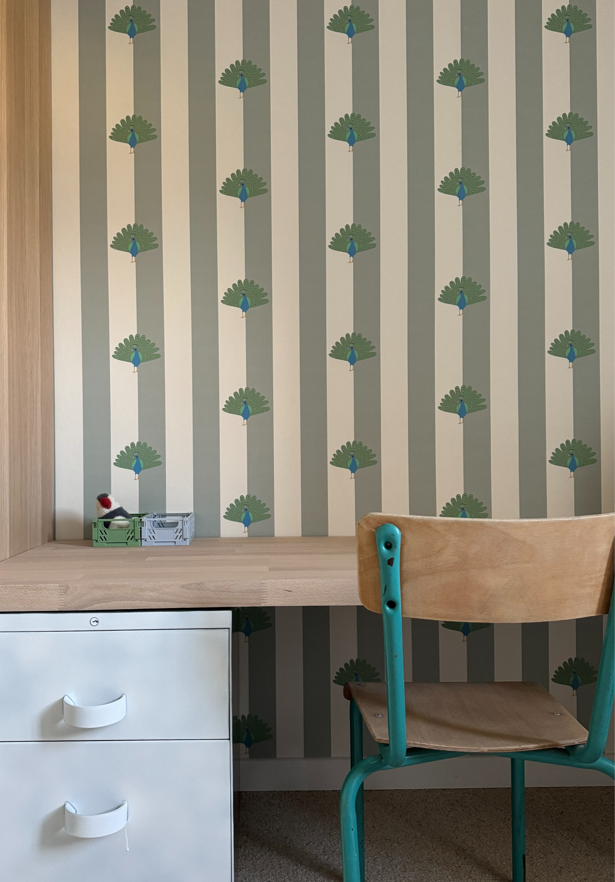 Papier peint Léon à rayures vertes et motifs de paons, posé dans un espace bureau avec une chaise vintage en bois et métal.