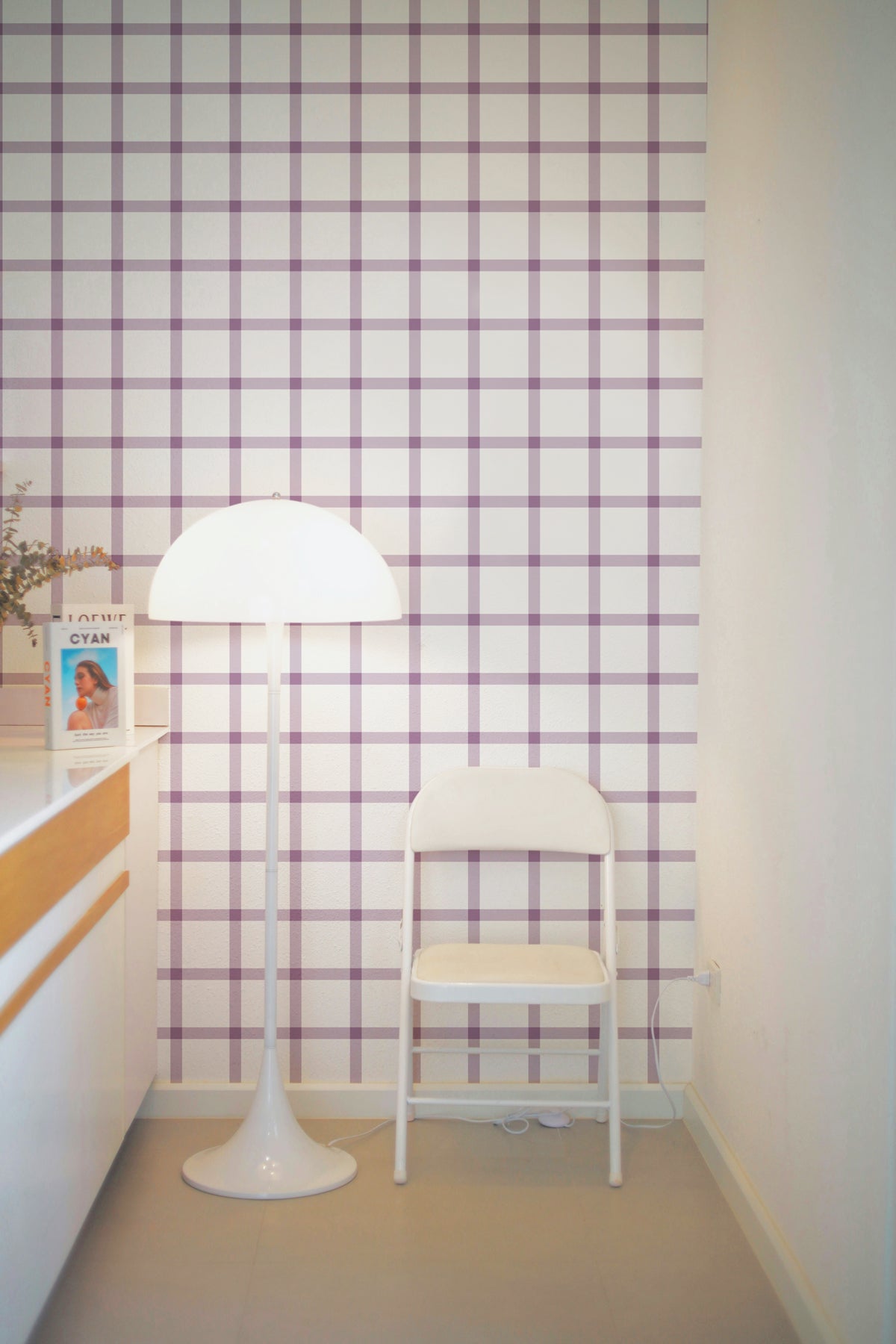 Papier peint Arielle à motif quadrillage lilas et blanc, posé dans un coin lumineux décoré avec un lampadaire design blanc et une chaise épurée.
