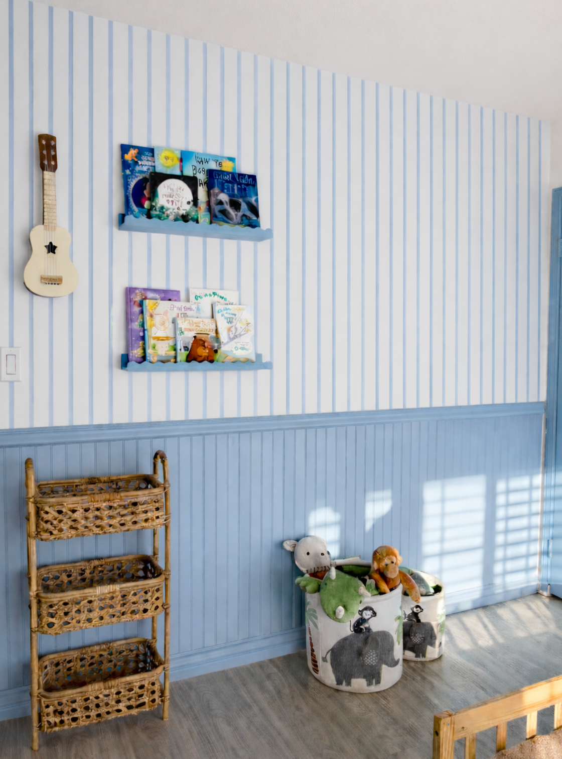 Papier peint Marine à rayures bleues au-dessus d'un soubassement bleu, avec étagères de livres, ukulélé et paniers de rangement.