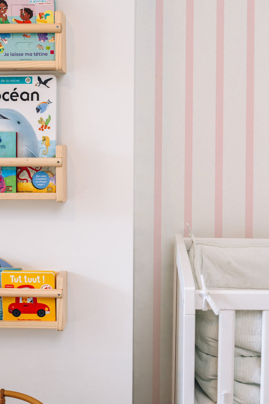 Papier peint Rosie à rayures roses, posé derrière des étagères à livres en bois et un lit d'enfant blanc.
