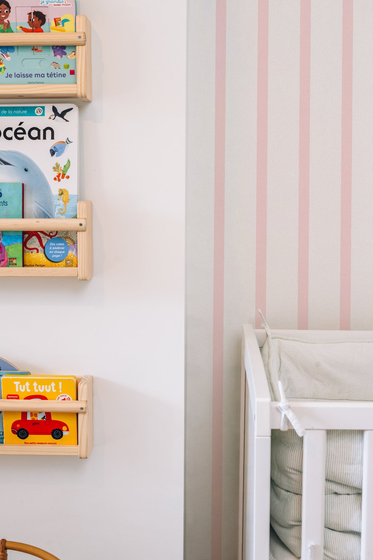 Papier peint Rosie à rayures roses, posé derrière des étagères à livres en bois et un lit d'enfant blanc.