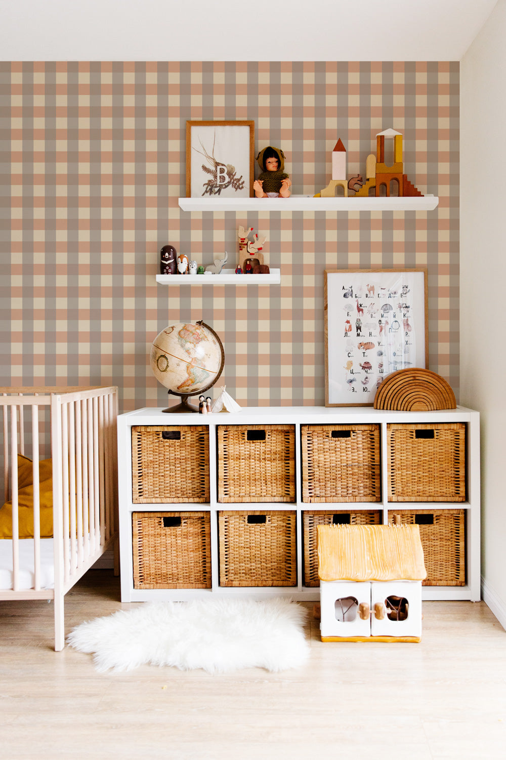 Papier peint Karl à motif vichy gris et marron, décorant une chambre de bébé chaleureuse avec un lit en bois, un grand meuble blanc avec des paniers de rangement en osier et des étagères murales décorées de jouets.